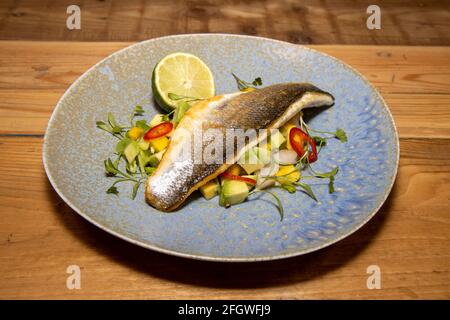 Ein köstlicher Teller Fisch Seebarsch mit Mango und Avocado Salsa auf einem hölzernen Küchentisch Stockfoto