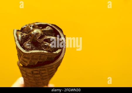 Schwarzes Eis in einem Waffelkegel auf gelbem Hintergrund. Stockfoto