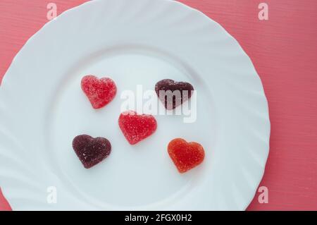 Herzförmige Marmelade auf einem weißen Teller rosa Hintergrund Nahaufnahme. Valentinstag-Konzept. Stockfoto