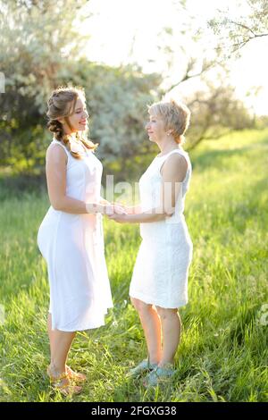 Kaukasisches Mädchen, das die Hände der Mutter nach draußen hält und weißes Kleid trägt. Stockfoto