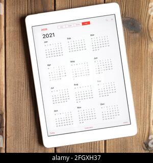 Eine Tablette mit einem offenen Kalender für 2021 Jahr auf einem Holzbrett Tisch Hintergrund. Quadrat Stockfoto