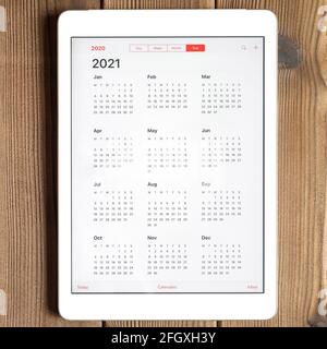 Eine Tablette mit einem offenen Kalender für 2021 Jahr auf einem Holzbrett Tisch Hintergrund. Quadrat Stockfoto