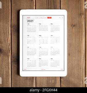 Eine Tablette mit einem offenen Kalender für 2021 Jahr auf einem Holzbrett Tisch Hintergrund. Quadrat Stockfoto
