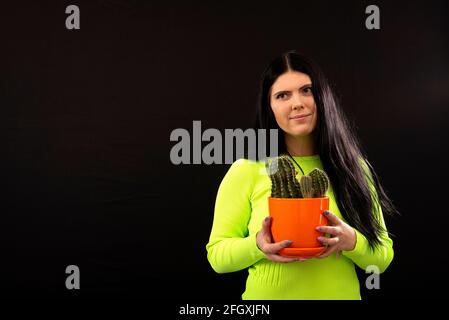 Porträt einer glücklichen jungen Frau, die Kaktus-Topfpflanze isoliert hält Auf schwarzem Hintergrund Stockfoto