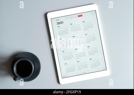 Ein Tablet mit einem offenen Kalender für 2021 Jahre und Eine Tasse Kaffee auf grauem Hintergrund Stockfoto