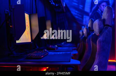 Im Inneren des Internetcafés, leuchtendes blaues Neonlicht, beleuchteter Cybercafe-Raum, Tische mit Computern, leere Stühle in Reihe, keine Menschen. Moderner Ort zum Spielen Stockfoto