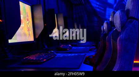 Im Inneren des Internetcafés, leuchtendes blaues Neonlicht, beleuchteter Cybercafe-Raum, Tische mit Computern, leere Stühle in Reihe, keine Menschen. Moderner Ort zum Spielen Stockfoto