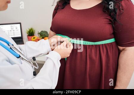Fettleibigkeit, ungesundes Gewicht. Ernährungsberaterin inspiziert die Taille einer Frau mit einem Meter-Band, um eine Gewichtsabnahme Diät zu verschreiben Stockfoto