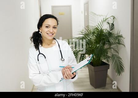 Arztberuf. Brünette Hausärztin mit Patientenakte in der Hand stehend in einer Klinik, Porträt Stockfoto