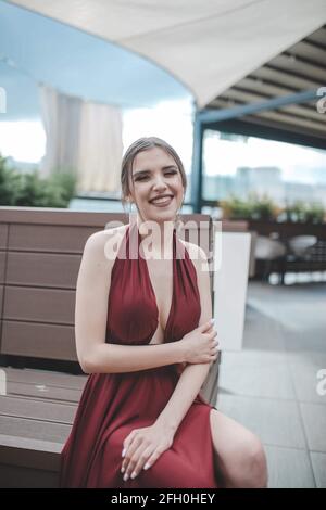 Ein flacher Fokus einer fröhlichen Frau, die einen stilvollen trägt Rotes Kleid in einem Restaurant im Freien Stockfoto