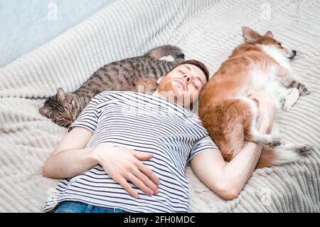 Ein junger Mann, eine Katze und ein Hund schlafen alle zusammen auf einem Bett. Stockfoto