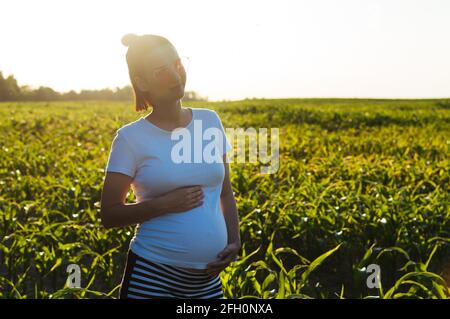 Schwanger glücklich junge Frau in der Sonne bei Sonnenuntergang auf Die Natur hält ihren Magen in den Händen und lächelt Stockfoto