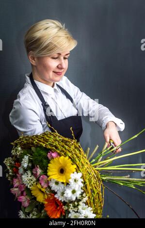 Große kreative Blumenstrauß Nahaufnahme auf einem grauen Hintergrund. Florist in den Prozess der Arbeit an einem Strauß. Vertikales Foto Stockfoto