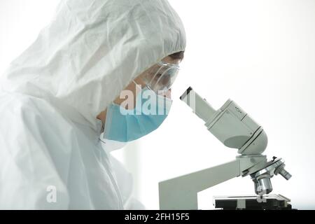 Arzt in einem Schutzanzug, der eine blaue Maske trägt Handschuhe in einem Labor schauen durch ein Mikroskop Stockfoto