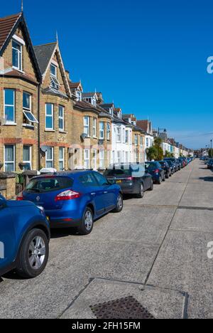 Wohnstraße von viktorianischen Reihenhäusern ohne Fahrten und Parken auf der Straße mit Autos, die entlang der Straßenlänge in West Sussex, England, Großbritannien, geparkt sind. Stockfoto