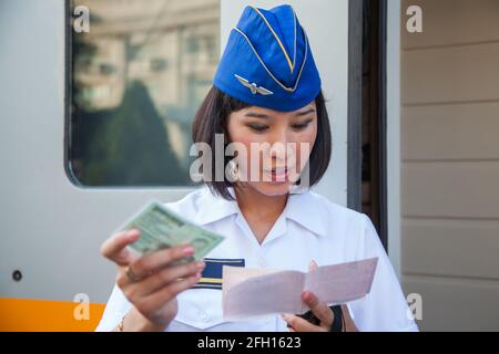 Almaty, Kasachstan - 06. Juni 2012: Schnellzug Talgo-Tulpar. Junge asiatische Zugwirtin in einer Garisson-Kappe beim Prüfen von Fahrkarten. Stockfoto