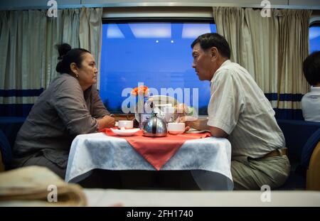 Almaty, Kasachstan - 06. Juni 2012: Schnellzug Talgo-Tulpar. Restaurant mit Speisewagen. Ein erwachsenes Paar trinkt Tee. Blaue Abendbeleuchtung. Stockfoto