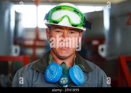 Golderz Bergbau- und Verarbeitungsanlage, Altynalmas Unternehmen. Asiatischer Arbeiter mit weißem Hardhut, Schutzbrille, Atemschutzmaske, die für Fotos posiert. Stockfoto