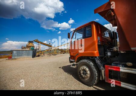 Bergbau- und Verarbeitungsanlage. Transport von Golderz zur Steinbrechmaschine. Orangefarbener LKW links. Region Almaty, Kasachstan Stockfoto