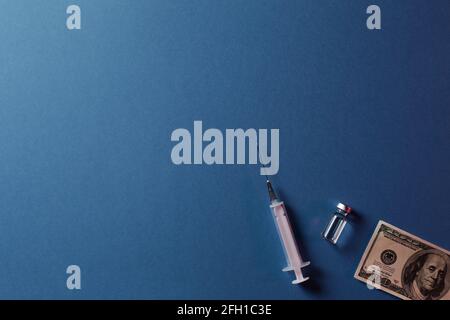 Fläschchen mit Coronavirus oder Covid-19-Impfstoff auf einem Stapel Von einhundert US-Dollar-Scheinen neben einer Spritze Und mehr Banknoten Stockfoto