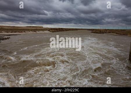 Region Kzylorda, Kasachstan. Aklak-Staudamm am Fluss Shardara. Turbulentes Wasser, stürmische Wolken, Panoramasicht. Stockfoto