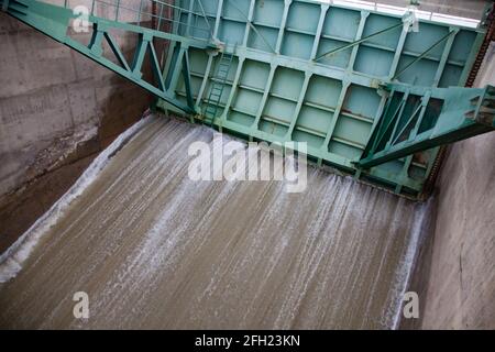 Aklak-Staudamm am Fluss Shardara. Halboffene Staumauer aus grünem Stahl. Starker Wasserstrahl. Kasachstan, Region Kzylorda. Stockfoto