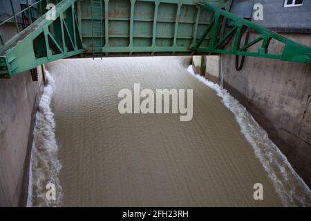 Aklak-Staudamm am Fluss Shardara. Öffnen Sie den grünen Metallwasserverschluss des Staudamms im Hochwasser. Ruhiger Wasserstrahl. Kyzylorda, Kasachstan. Stockfoto