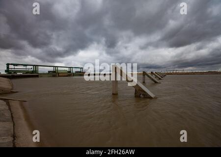 Aklak-Staudamm am Fluss Shardara. Betonbrecher im Kanal. Wasserblenden links. Graue, stürmische Wolken. Kasachstan, Region Kzylorda. Stockfoto