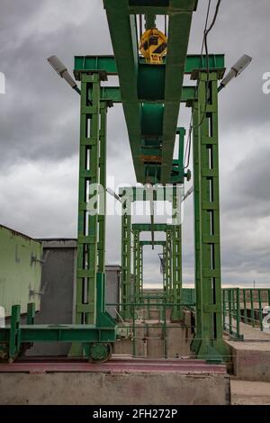 Aklak-Staudamm am Fluss Shardara. Hebevorrichtung von Metallgewichten für Wasserverschluss. Elektrokran auf Schienen. Grauer Sturmhimmel. Kasachstan, Region Kzylorda. Stockfoto