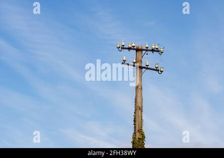 Low-Angle-Ansicht des alten und verfallenden Telegrafepostens an einem Bahnhof in Deutschland gegen blauen Himmel mit Zirruswolken. Selektiver Fokus auf den Vordergrund. Stockfoto
