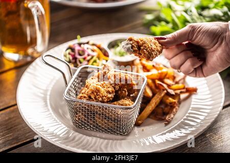 Weibliche Hand hält ein gebratenes Hähnchen Nugget in einer weißen Sauce über einem Teller mit pommes frites und Salat getaucht. Stockfoto