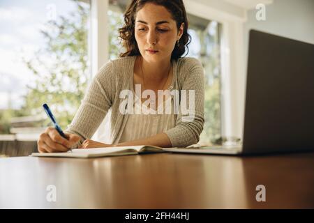 Schöne Frau, die am Laptop arbeitet und Notizen schreibt. Geschäftsfrau, die vom Home Office aus arbeitet. Stockfoto