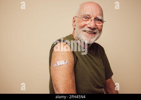 Porträt eines älteren Mannes, der lächelte, nachdem er eine Impfung erhalten hatte. Reifer Mann, der nach der Impfung seinen Arm mit Verband zeigt. Stockfoto