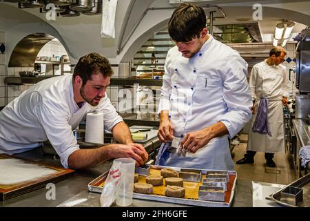 Zwei Köche bereiten Teigstücke in runden Metallringen auf einem Backblech zu, während der mit einem Michelin-Stern ausgezeichnete Koch Thomas Kellermann im Hintergrund steht, in der Küche von Schloss Wernberg, Wernberg-Köblitz, Oberpfalz, Deutschland. Kellermann verließ Schloss Wernberg Ende Mai 2018; Robert Morgan, zuvor Souschef und Kopfpastetenchef, übernahm dann die Leitung der Küche. Stockfoto