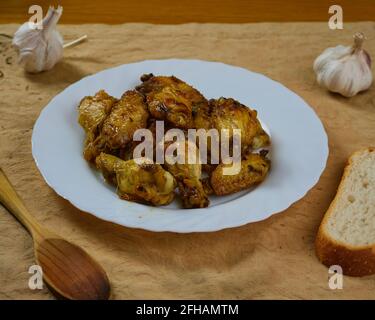 Knoblauch-Hühnerflügel (Pollo al ajillo). Spanisches Tapas-Gericht, serviert mit knusprigem Brot und seinen Zutaten auf einer braunen Serviette. Stockfoto
