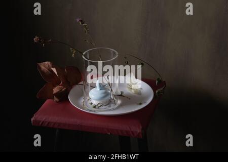 Vase mit Dekor und verblassten Blumen auf runder Platte Mit Feder auf grauem Hintergrund Stockfoto
