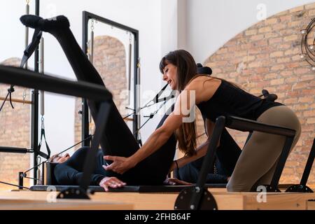Flexible weibliche Stretching Beine mit Hilfe von persönlichen Lehrer während Übungen auf Pilates Reformer Stockfoto