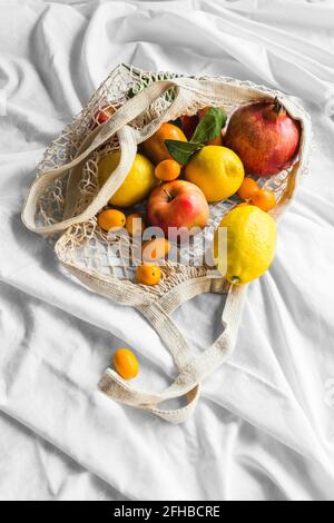 Von oben von verschiedenen ganzen reifen Apfel mit Zitronen in der Nähe Granatapfel und Kumquats in Öko-Beutel auf geknickelten Tuch Stockfoto