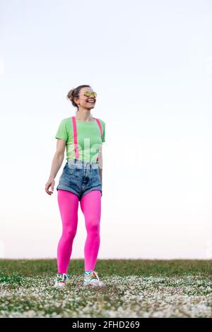 Ganzkörper entzückten junge Frauen in Shorts und leuchtendem Pink Strumpfhosen laufen fröhlich auf üppiger, grasbewachsener Lichtung in der Natur Stockfoto