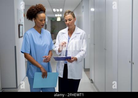 Zwei verschiedene Ärztinnen, die im Krankenhausflur stehen und sie betrachten Dokument mit medizinischen Diagrammen Stockfoto