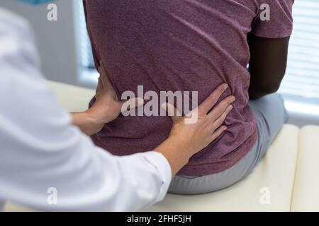 Mittelteil der kaukasischen Physiotherapeutin, die sich nach hinten in den afroamerikanischen bereich einkastelt Männlicher Patient Stockfoto