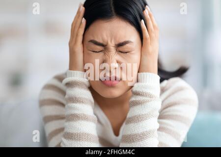 Emotionale Asiatische Frau, Die Zu Hause Die Ohren Mit Den Händen Bedeckt Stockfoto