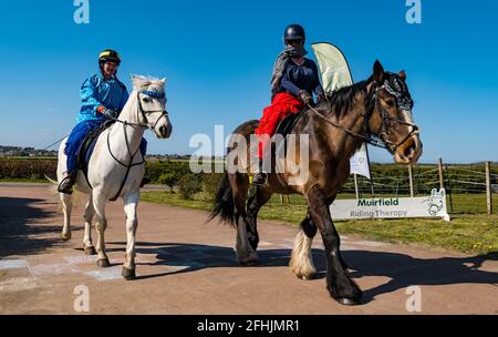 East Lothian, Schottland, Großbritannien, 25. April 2021. Virtueller Kilt Walk: Kilt Walker, die die Muirfield Riding Therapy Charity unterstützen, überqueren eine ‘Ziellinie’, um ihre Teilnahme an ihrer Spendenaktion ‘Round the World’ zu feiern. Im Bild: Morven McLelland auf Johnny & Charity, Therapiepferde unter Beccy O'Connor. Die Frauen und Pferde sind in arabischem Kostüm gekleidet, um die zurückgelegte Strecke darzustellen Stockfoto