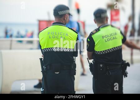 Spanische Polizeieinheit, Rückansicht mit Logo der lokalen Polizei auf Uniform, Aufrechterhaltung der öffentlichen Ordnung in den Straßen von Alicante, Spanien Stockfoto