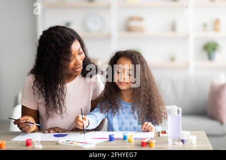 Porträt einer glücklichen schwarzen Mutter und ihrer Tochter, die zu Hause mit Aquarellen und Gouache malte. Konzept für Familienhobys Stockfoto