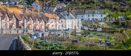 Panoramablick auf eine Reihe von charmanten Reihenhäusern auf einem Hügel, die am 19. April zum Beer Beach mit Zuteilungen vor dem Hotel in Beer, Devon, Großbritannien, führen Stockfoto