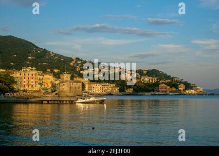 Ruhiges ligurisches Meer an der Küste von Rapallo. An Land und hinter der Burg werden auf einem bewaldeten Hügel Gebäude errichtet. Stockfoto