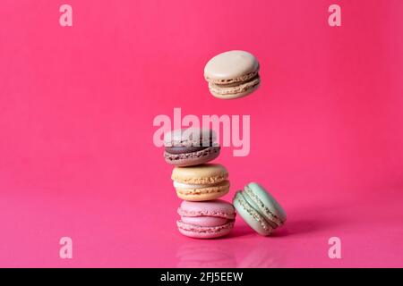 Süße französische Makronen, die auf rotem Hintergrund in Bewegung fallen. Pastellfarbene fliegende Makronen-Kekse. Essen und Kulinarik. Stockfoto