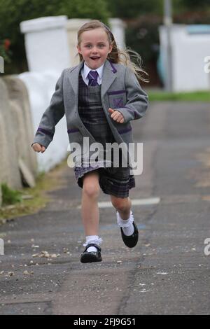 Ayrshire, Schottland, 20. August 2018. Erster Tag der Grundschule .kleines Mädchen läuft auf dem Bürgersteig in neuer Schuluniform Stockfoto