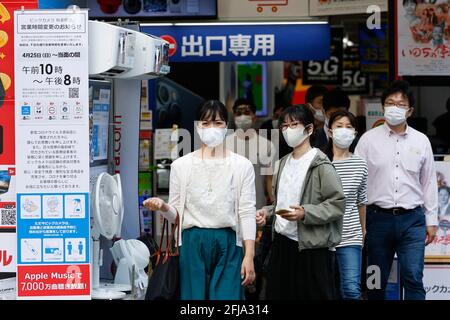 Tokio, Japan. April 2021. Menschen mit Gesichtsmasken kommen an einem Schild vorbei, auf dem die Geschäftszeiten im Rahmen des neuen Ausnahmezustands in Tokio angekündigt werden. Der dritte Ausnahmezustand begann heute, vom 25. April bis zum 11. Mai, in Tokio, Osaka, Kyoto und Hyogo, um Infektionen von Coronavirus-Fällen einzudämmen. Quelle: Rodrigo Reyes Marin/ZUMA Wire/Alamy Live News Stockfoto